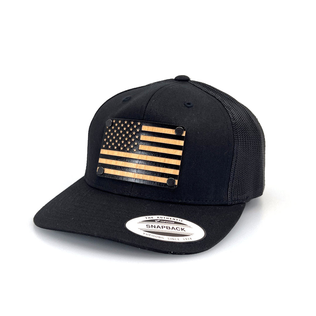 A solid wood, patch of the American flag riveted to a black snapback trucker hat.