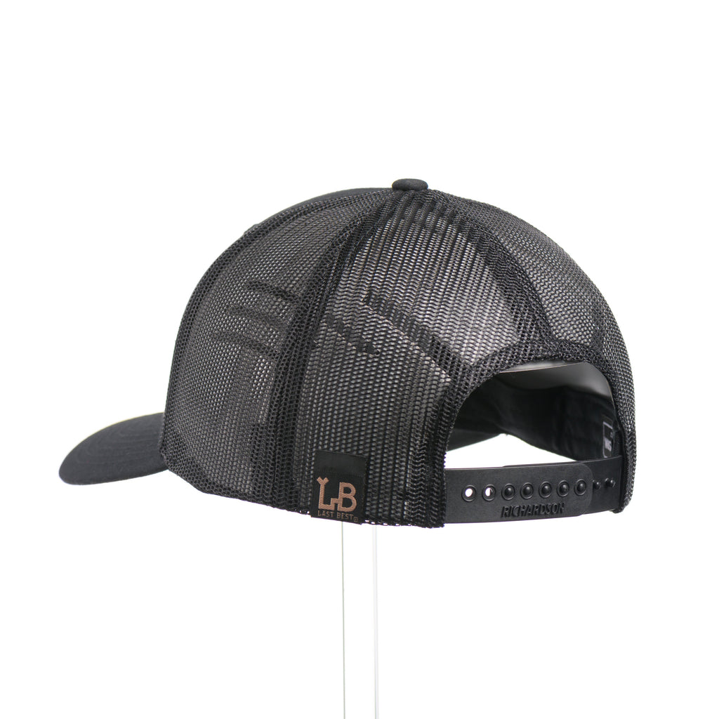 The back of a black Richardson trucker hat with an etched mahogany wood triangle camping patch on a green metal plate.