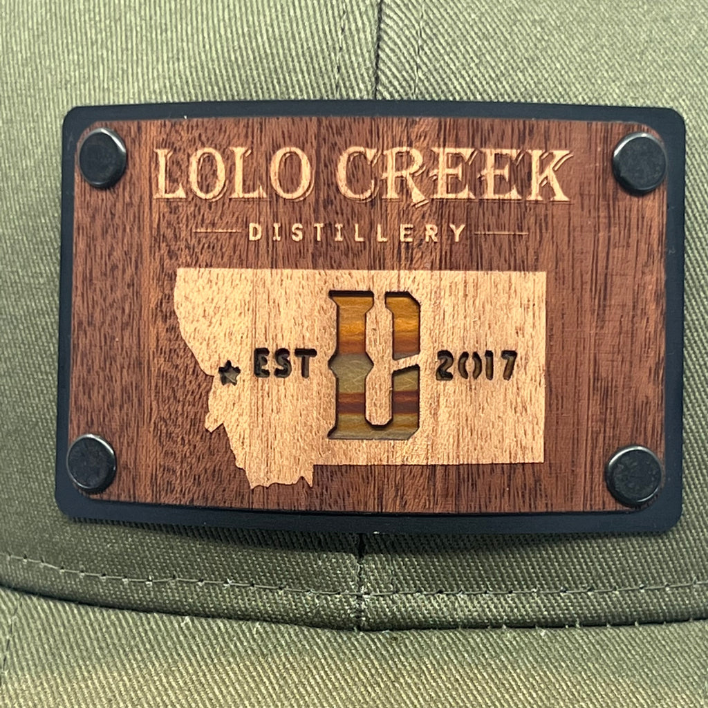 A close up of a mahogany wood patch with copper inlay featuring the logo of Lolo Creek Distillery