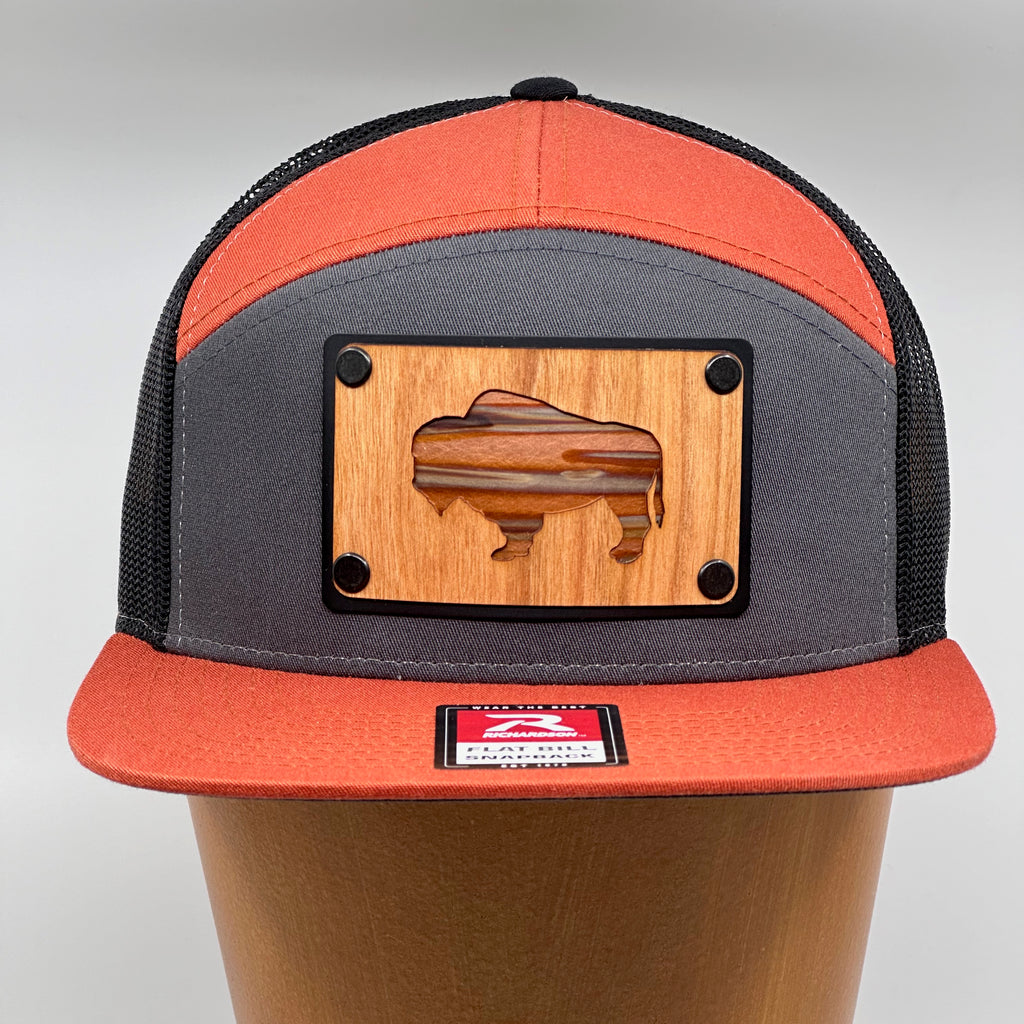 A bison silhouette cherry wood and copper plate patch riveted to a orange and gray Richardson flat bill.