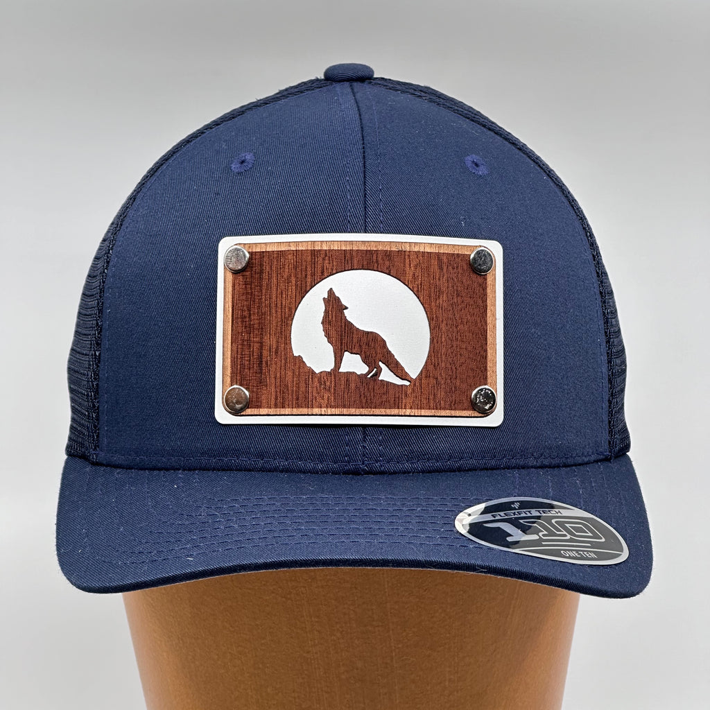 A wolf howling at the moon on a mahogany and aluminum wood plate patch riveted to a navy trucker hat.