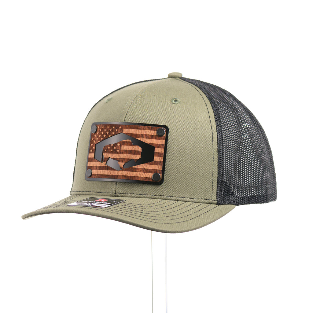 A loden green and black mesh Richardson trucker hat with an etched walnut wood American flag and bison cut out on a black metal patch at a quarter turn.