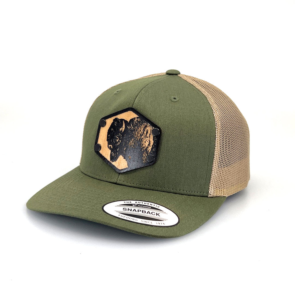 A solid wood patch of a bison head riveted to an olive green and khaki trucker hat.